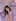 Little girl with a purple hair clip sitting on a lavender gingham bed between purple plush toys