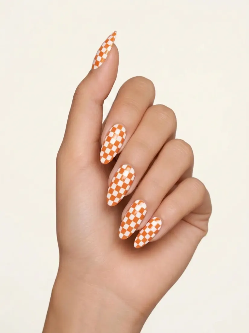 Hand with long almond nails painted in an orange checkerboard pattern