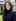 A real estate agent in a navy blazer stands on a covered porch in an AI realtor headshot.