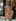 A blonde woman in a white camisole and jeans rests her chin on her hand at a cafe table, before the Superhero Generator restyles the portrait.