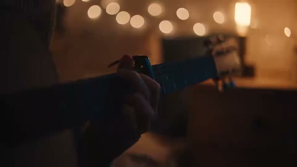 An AI video of hands fretting chords on a blue guitar neck in a dim room lit by warm string lights.