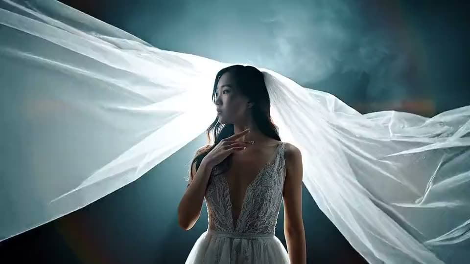 An AI video of a bride in a lace gown standing in a backlit haze as her long white veil billows out on both sides.