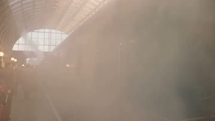 Sunlight streaming through haze under the arched glass roof of a train station.