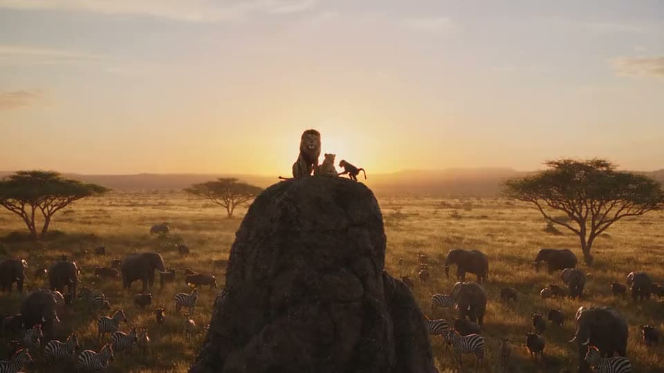An AI video of a lion, a cub and a baboon atop a tall rock at sunset above a savanna full of elephants and zebras.