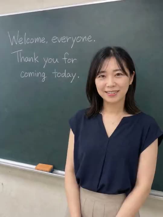 A vertical AI video of a smiling teacher at a chalkboard that reads "Welcome, everyone. Thank you for coming today."