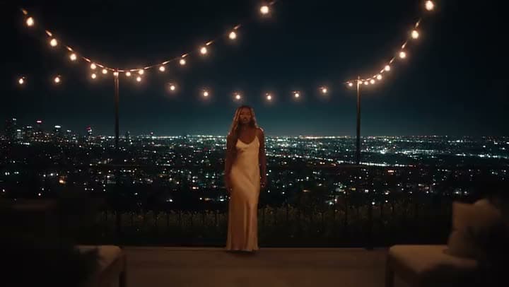 A woman on a terrace at night with city lights behind her.