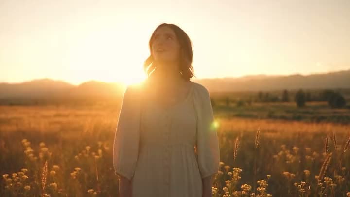 A woman standing in a golden field in warm evening light.