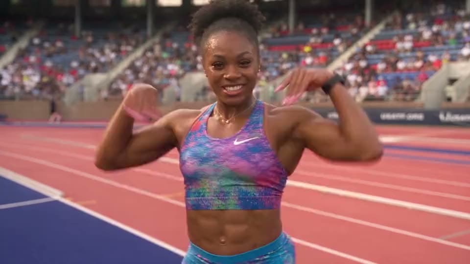 An AI video of a smiling sprinter in a Nike sports top flexing her arms on a red running track in front of a packed stadium.
