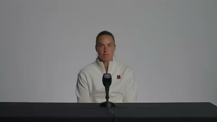An AI video of a female tennis player in a white jacket seated at a press conference table behind a single microphone.