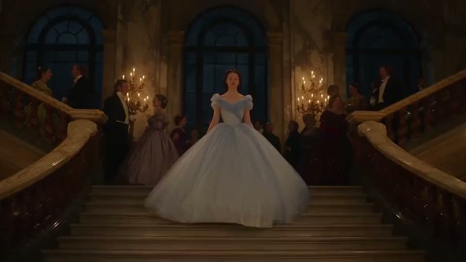 An AI video of a young woman in a pale blue ball gown descending a grand palace staircase as candlelit guests look on.