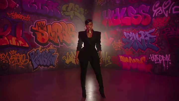 An AI music video of a woman in a black suit standing in a dim room lined with neon graffiti walls.