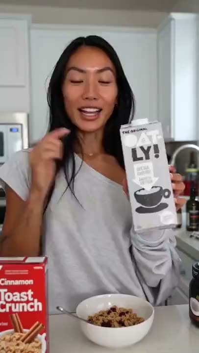 A vertical AI video of a woman in a kitchen holding up a carton of Oatly oat milk beside a bowl of cereal.
