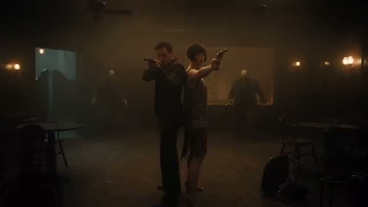 An AI video of a couple in 1920s clothes standing back to back with pistols raised as zombies close in on a dim speakeasy.