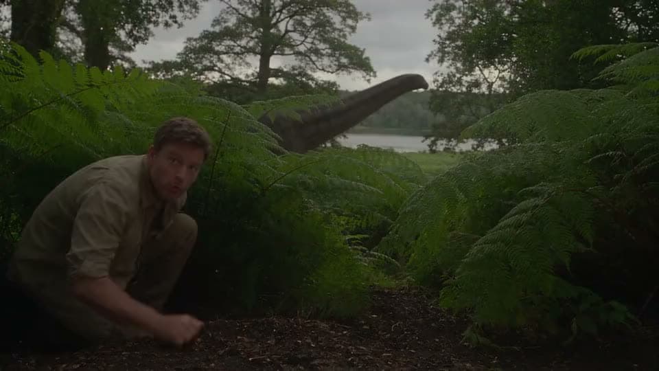 An AI video of a man crouching in ferns by a lake as the long neck of a sauropod dinosaur rises behind the trees.