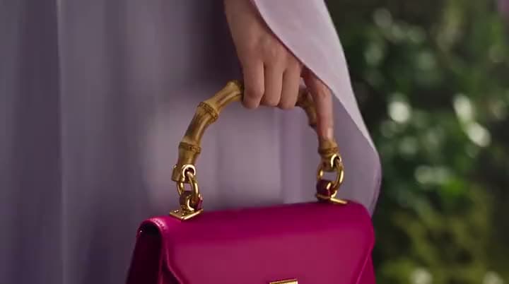 An AI product ad of a hand in a lilac sleeve holding a magenta leather handbag by its gold bamboo-style handle.