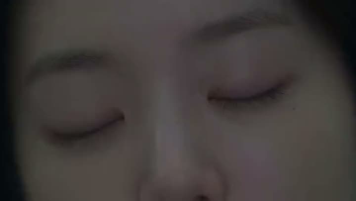 An AI video close-up of a young woman's face with her eyes closed, lying still in dim, low light.