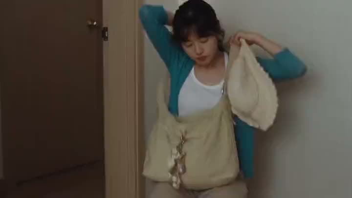 An AI video of a young woman in a teal cardigan pulling a canvas tote bag over her shoulder in a narrow hallway.